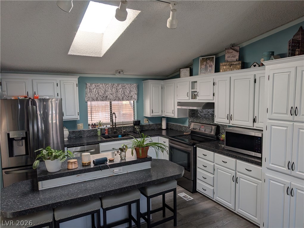 320 6th Street Panaca, NV 89042 - Photo 11 of 30 Kitchen with a skylight, stainless steel appliances, white cabinetry, and a kitchen breakfast bar