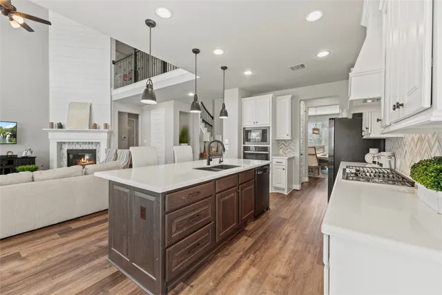 a kitchen with stainless steel appliances granite countertop a stove top oven a sink dishwasher and a refrigerator with wooden floor