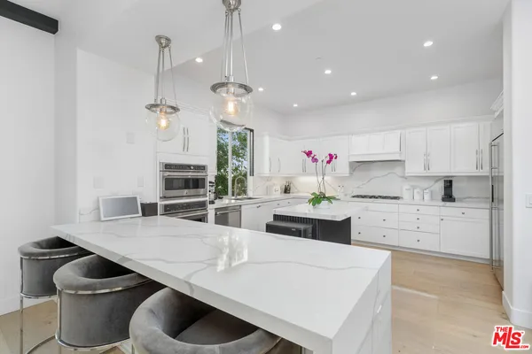 a kitchen with stainless steel appliances kitchen island granite countertop a stove a sink a refrigerator and white cabinets with wooden floor
