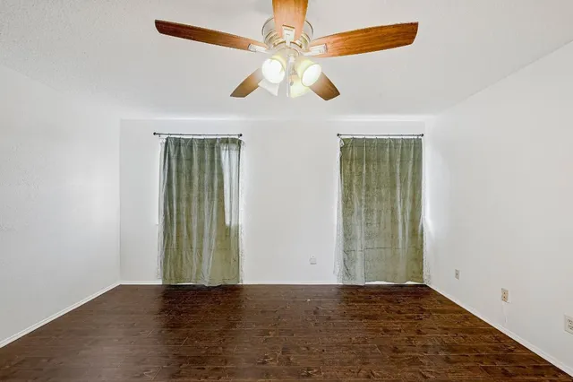 an empty room with wooden floor chandelier fan and windows