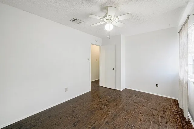 an empty room with a chandelier fan and wooden floor