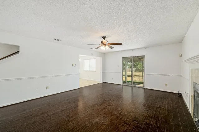 an empty room with wooden floor chandelier fan and windows
