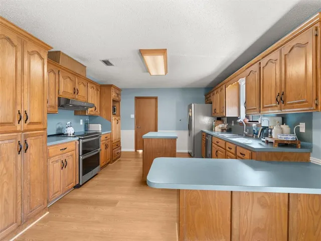 a kitchen with stainless steel appliances granite countertop a stove a sink a refrigerator and blue cabinets with wooden floor