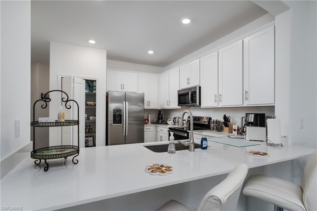 2140 Dragonfruit Way Naples, FL 34120 - Photo 5 of 35 a kitchen with stainless steel appliances a sink a stove a refrigerator cabinets and chairs