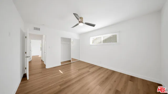 an empty room with wooden floor and ceiling fan