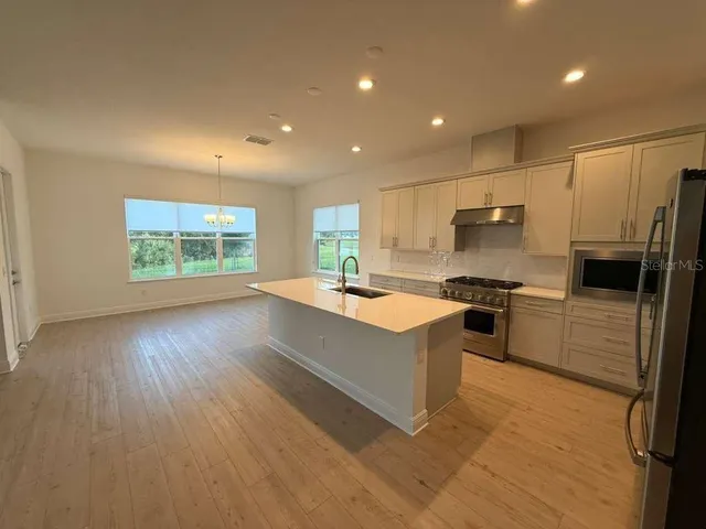 a large kitchen with stainless steel appliances a large counter top a stove a sink dishwasher and a refrigerator with wooden floor