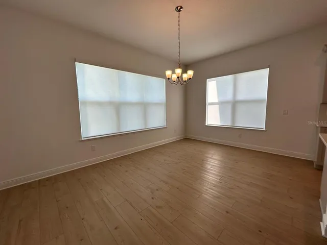 an empty room with wooden floor chandelier and windows