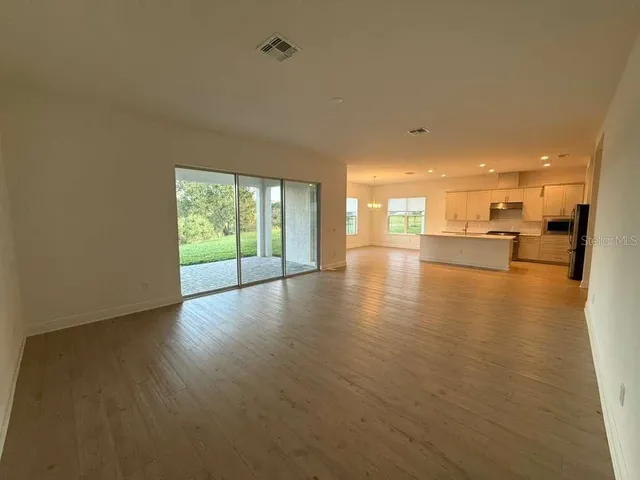 a view of an empty room and kitchen view with wooden floor
