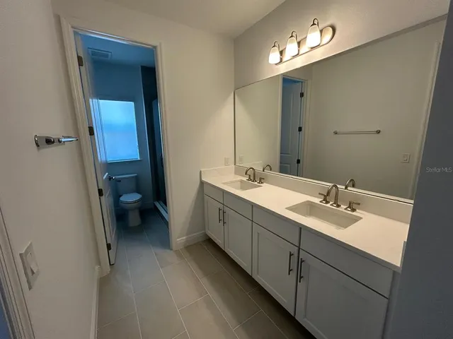 a spacious bathroom with a double vanity sink a toilet and a mirror