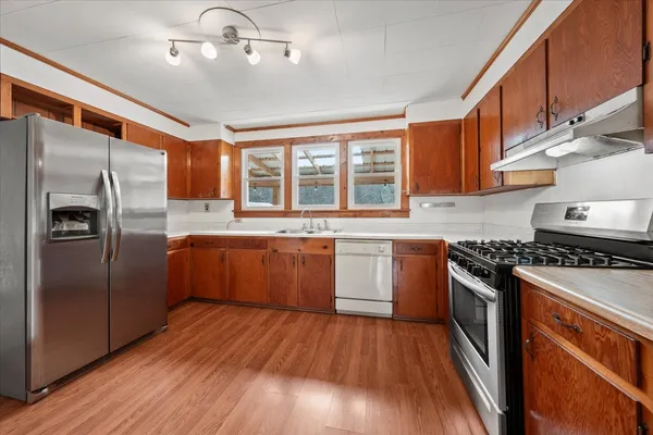 a kitchen with stainless steel appliances granite countertop a stove a sink dishwasher a refrigerator and wooden floor