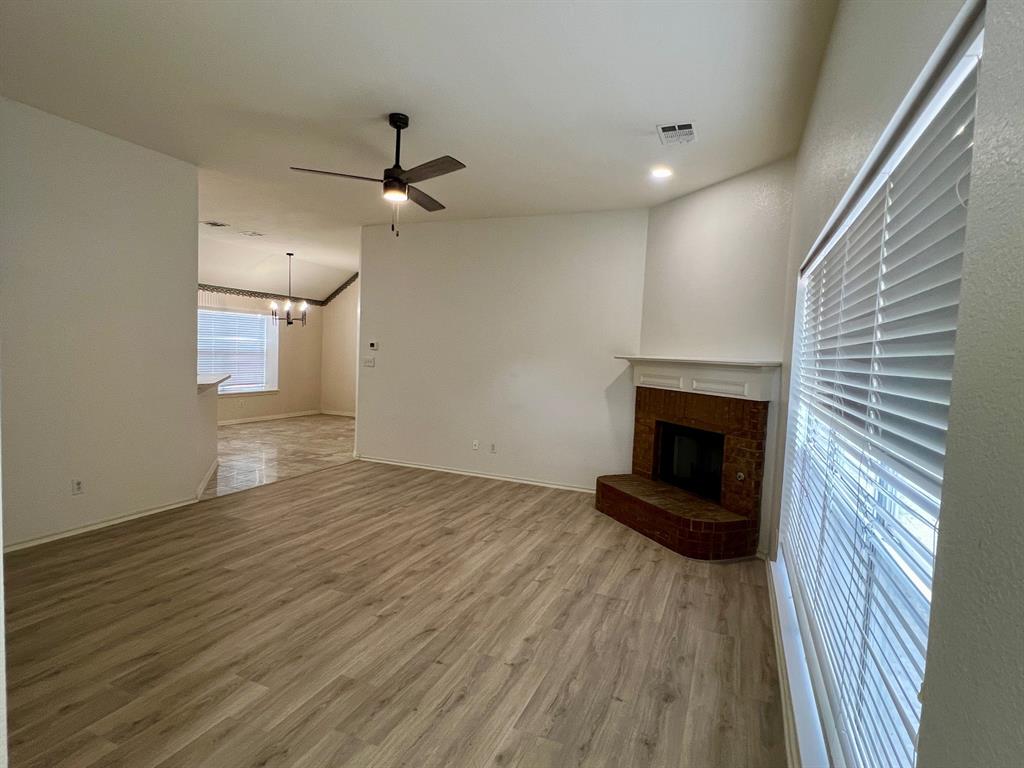 1348 Riley Drive Carrollton, TX 75007 - Photo 2 of 11 an empty room with wooden floor a ceiling fan a fireplace and windows