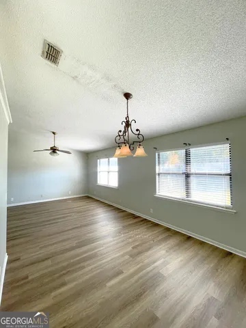 an empty room with wooden floor chandelier and windows