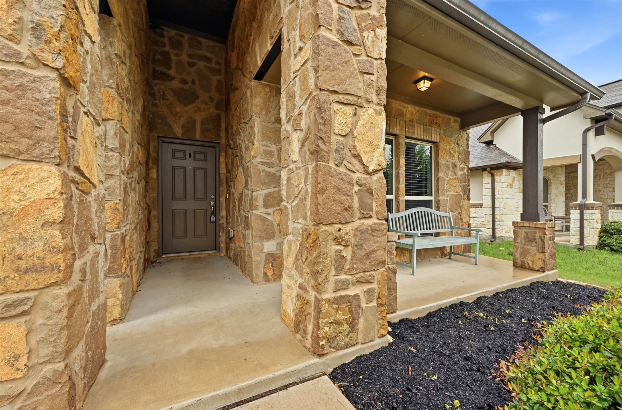 13116 Alans Way Manchaca, TX 78652 - Photo 2 of 25 Stone veneer exterior featuring a covered entry, dark paneled front door, an exterior light fixture, and a window with blinds