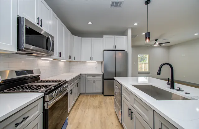 a kitchen with stainless steel appliances a sink dishwasher a refrigerator microwave and stove with wooden floor