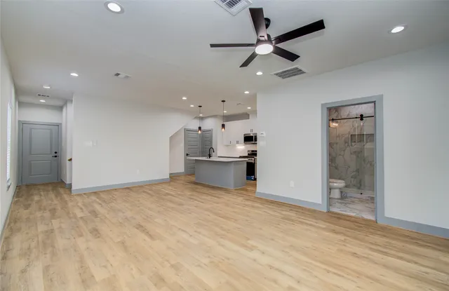 an empty room with wooden floor a ceiling fan and kitchen view