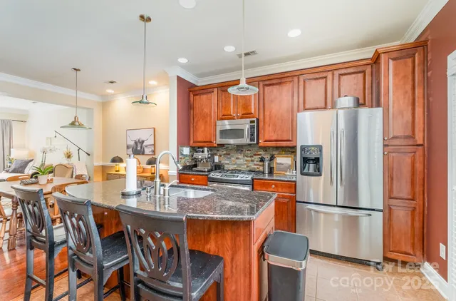 a kitchen with stainless steel appliances granite countertop a refrigerator a stove a sink a dining table and chairs