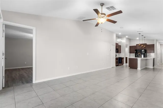 a view of an empty room and kitchen view with a ceiling fan