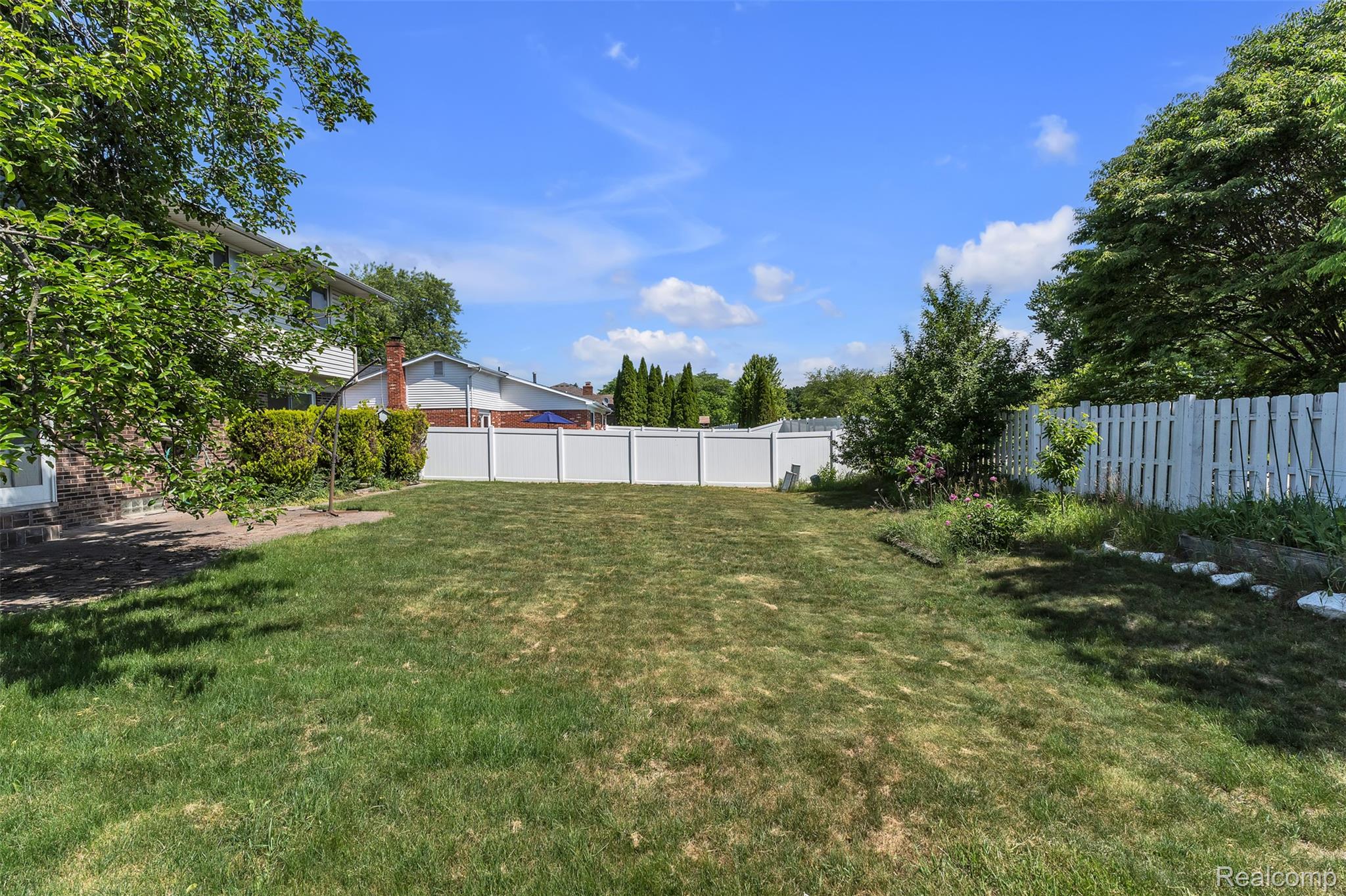 7000 Woonsocket Street Canton, MI 48187 - Photo 65 of 65 Expansive grassy backyard featuring a white privacy fence, mature trees, and shrubs