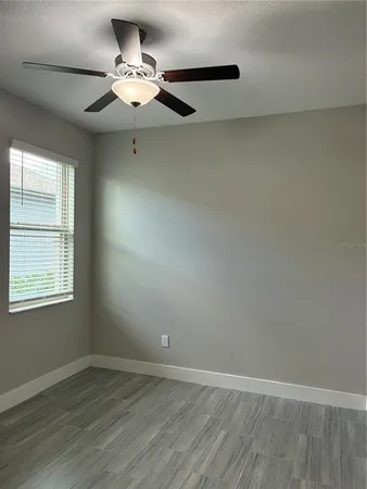 an empty room with wooden floor fan and windows