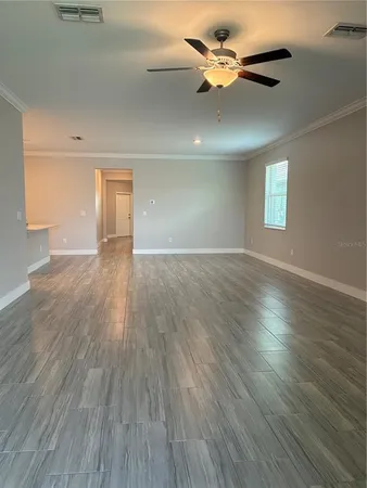 an empty room with wooden floor chandelier fan and windows