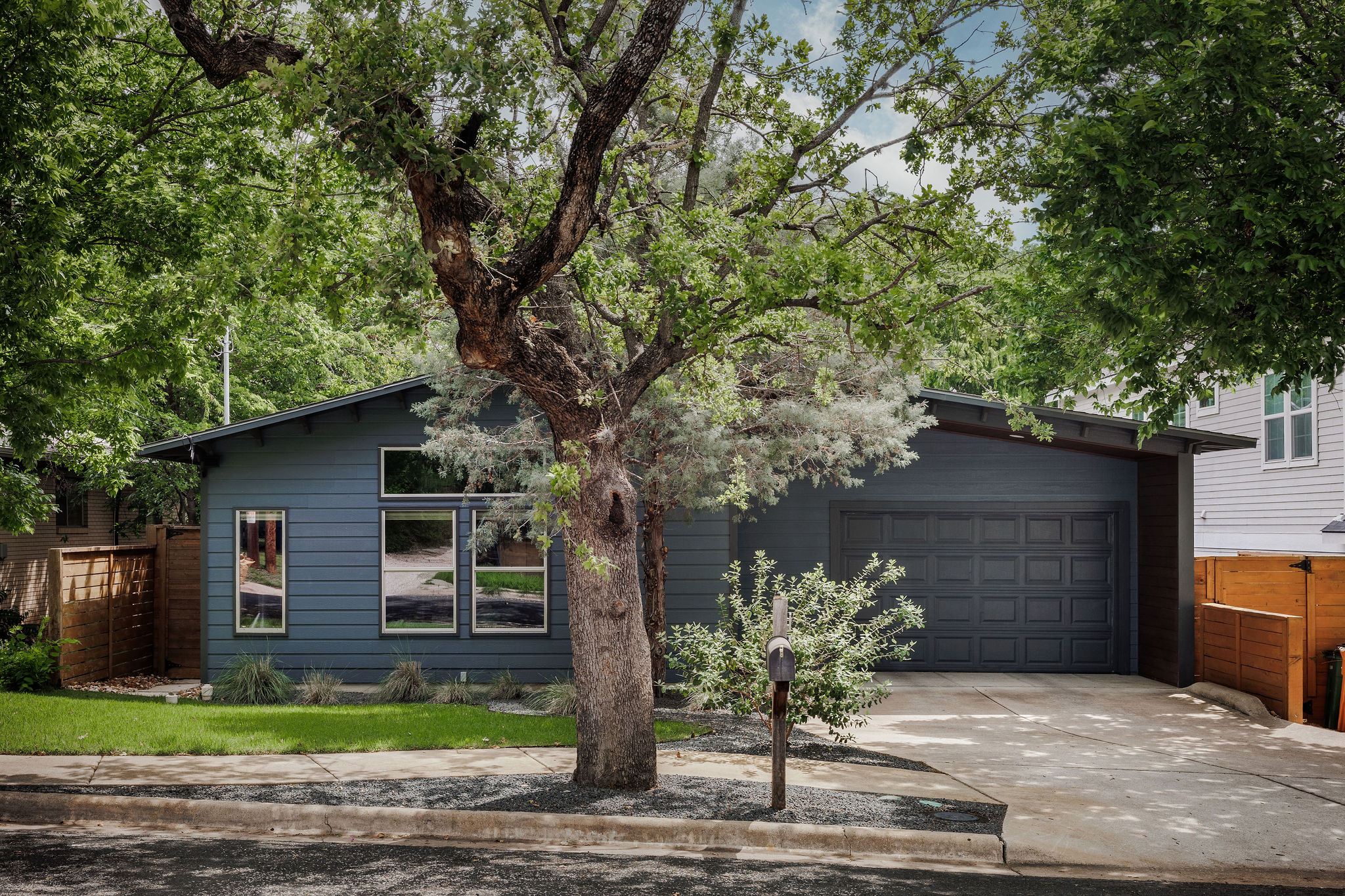 Contemporary single-story residence with a dark blue siding exterior, a dark gray garage door, and a concrete driveway