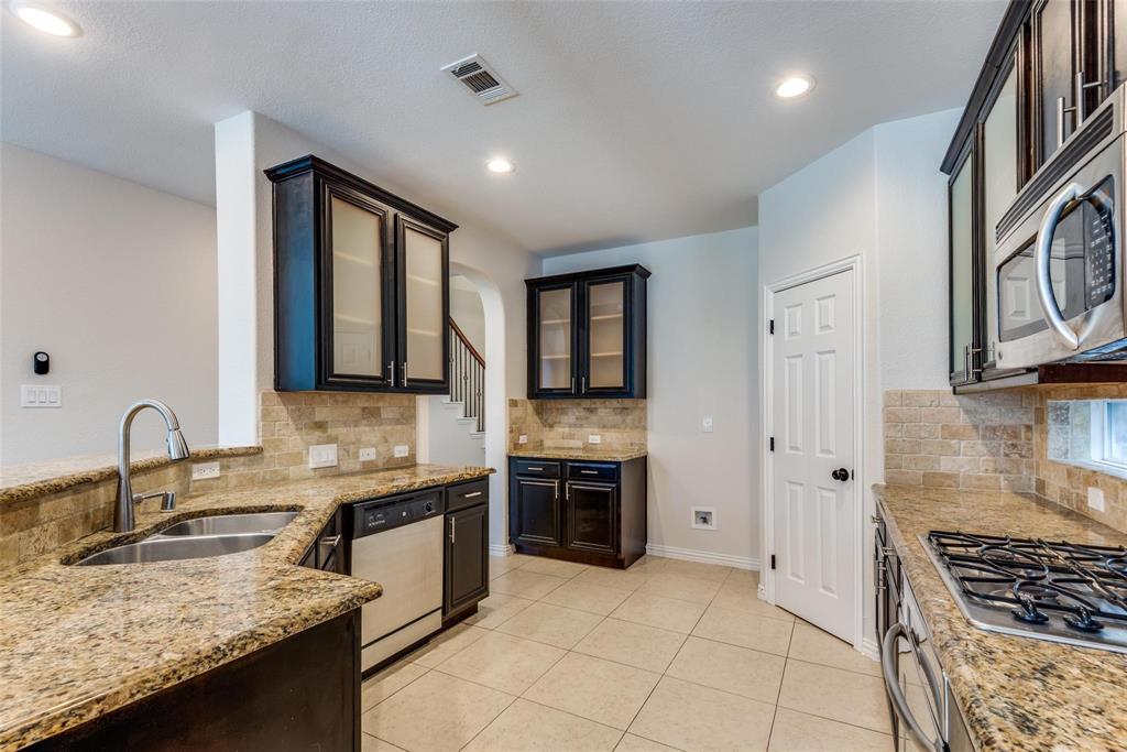 2344 Ranchview Drive Little Elm, TX 75068 - Photo 10 of 24 Kitchen featuring tile flooring, granite countertops, dark wood cabinetry with some glass-front doors, stainless steel appliances, and a tiled backsplash