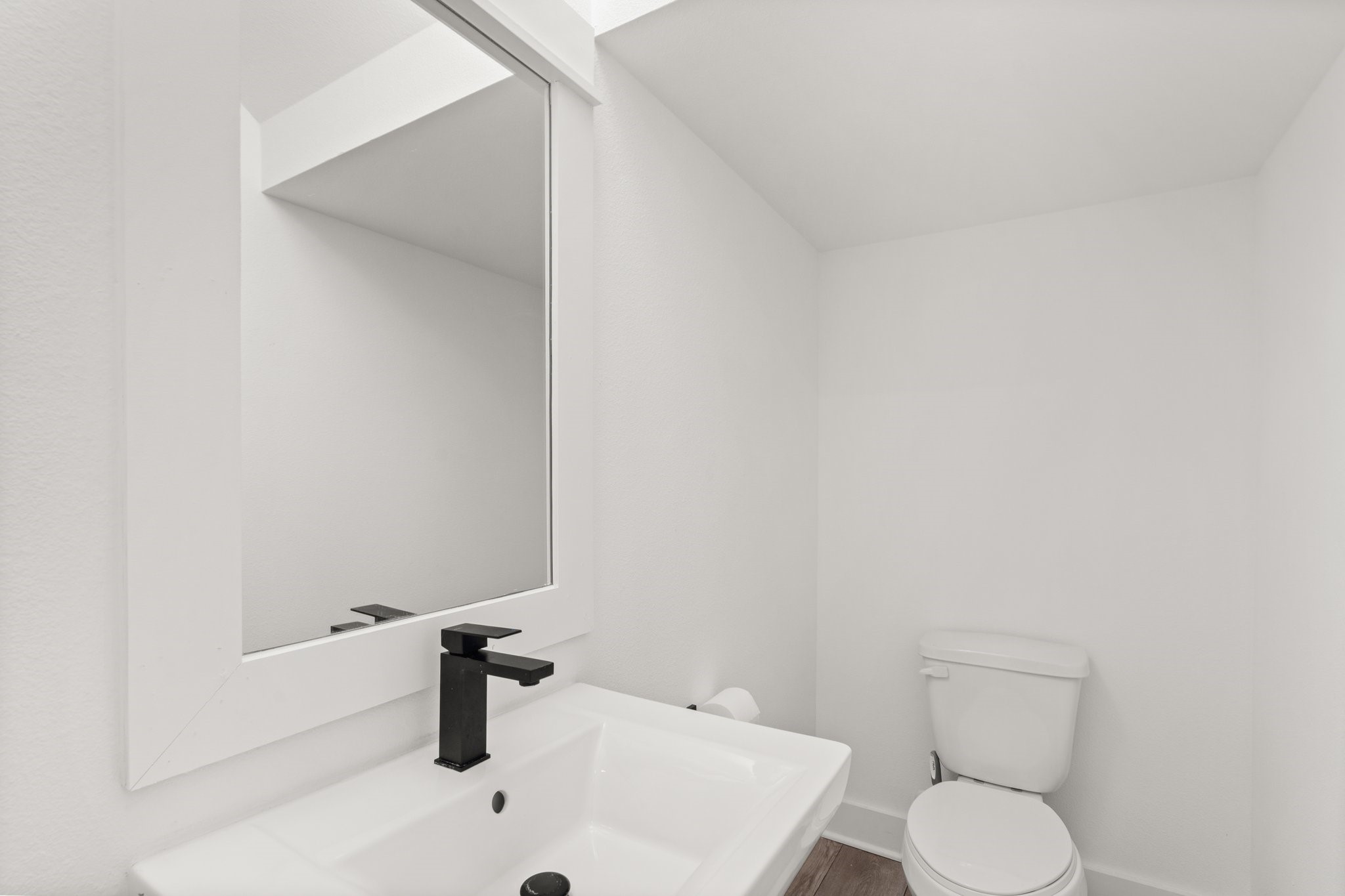 2928 Stevens Street Houston, TX 77026 - Photo 10 of 30 This photo showcases a modern, minimalist bathroom with a white sink and a sleek black faucet, a large mirror, and a toilet. The bright, clean design creates a fresh and inviting space.