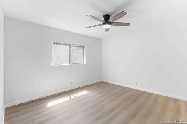 an empty room with wooden floor fan and windows