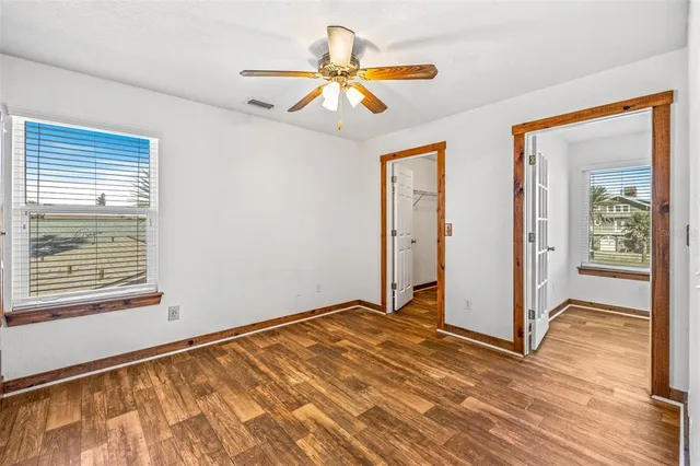 an empty room with a chandelier fan and wooden floor