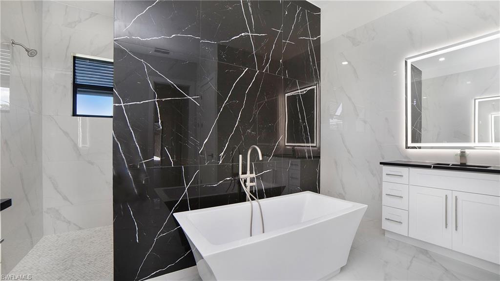 2343 Oil Well Road Naples, FL 34120 - Photo 17 of 46 Contemporary bathroom featuring a freestanding soaking tub, a black tiled accent wall, and a custom vanity with an illuminated mirror