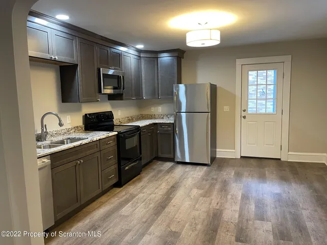 a kitchen with stainless steel appliances granite countertop a refrigerator a sink dishwasher a stove and white countertops with wooden floor