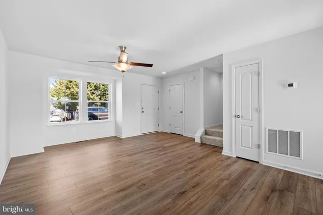 an empty room with wooden floor chandelier fan and windows