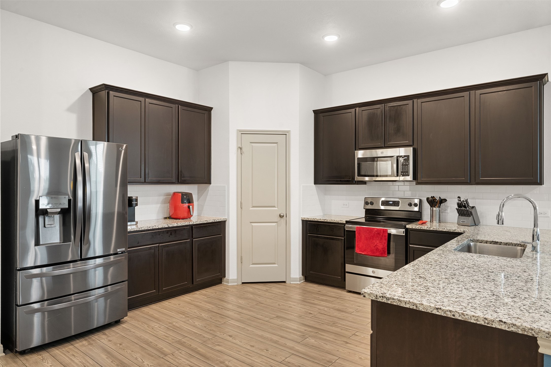 1968 Chief Street Bryan, TX 77807 - Photo 4 of 27 This kitchen features modern stainless steel appliances, dark wood cabinetry, and granite countertops. The space is well-lit with recessed lighting and has a functional layout, including a pantry and a double-door refrigerator.