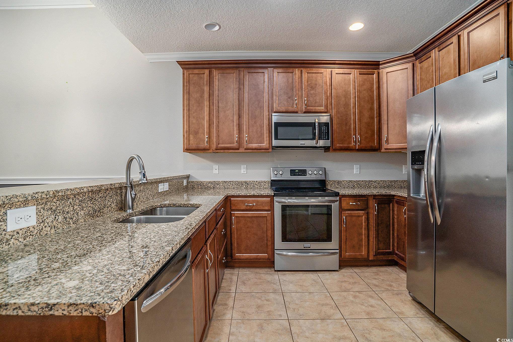 1018 Red Sky Lane, Unit 101 Murrells Inlet, SC 29576 - Photo 14 of 35 Kitchen featuring stainless steel appliances, light stone counters, a textured ceiling, light tile patterned floors, and brown cabinets