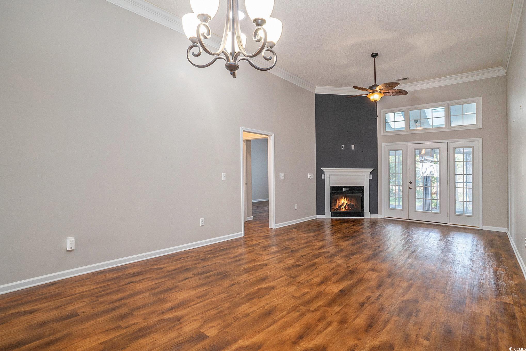 1018 Red Sky Lane, Unit 101 Murrells Inlet, SC 29576 - Photo 15 of 35 Unfurnished living room featuring a towering ceiling, a glass covered fireplace, ornamental molding, ceiling fan, and dark wood-type flooring