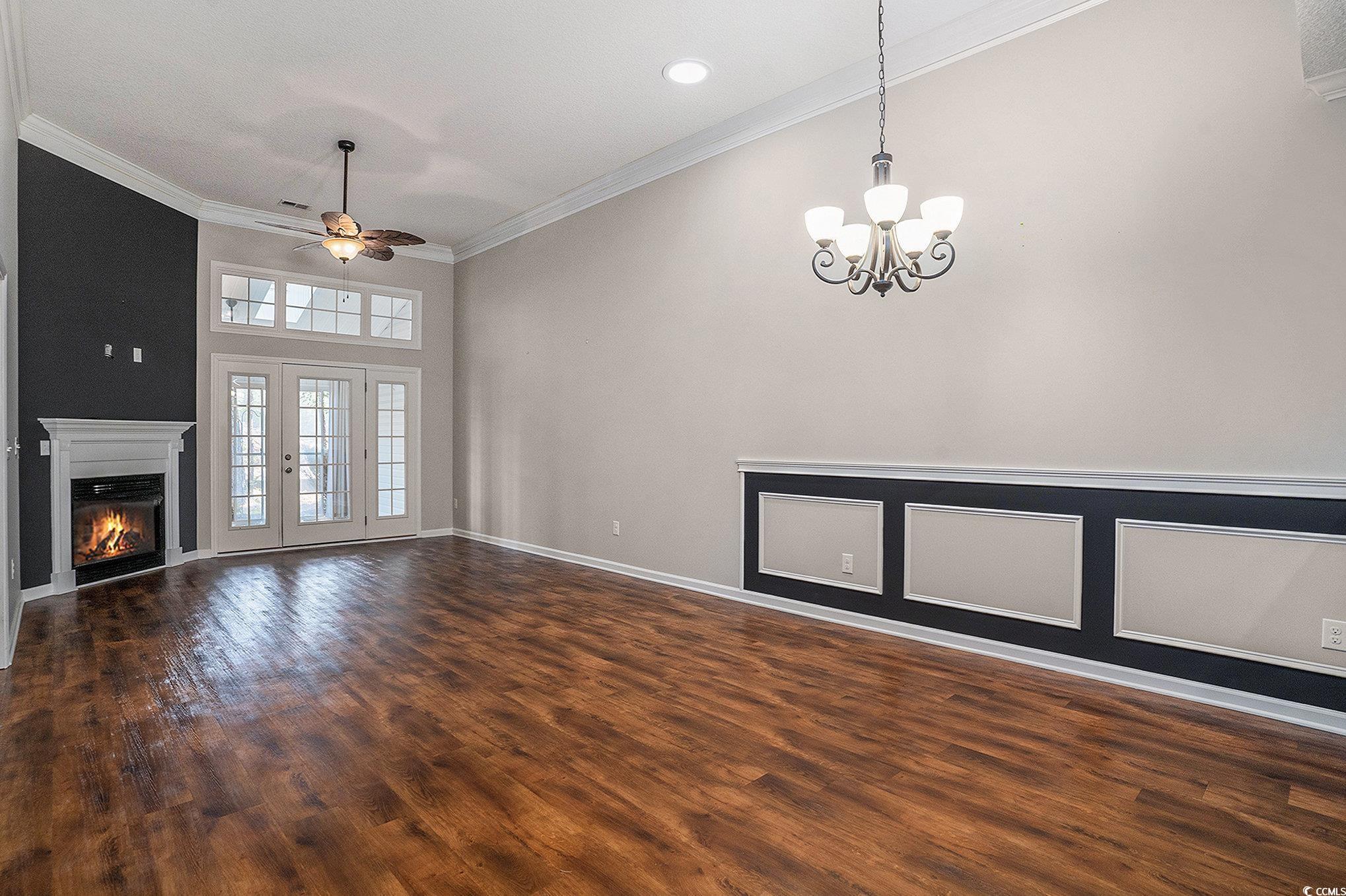 1018 Red Sky Lane, Unit 101 Murrells Inlet, SC 29576 - Photo 16 of 35 Unfurnished living room featuring dark wood-style flooring, a glass covered fireplace, a ceiling fan, crown molding, and a chandelier