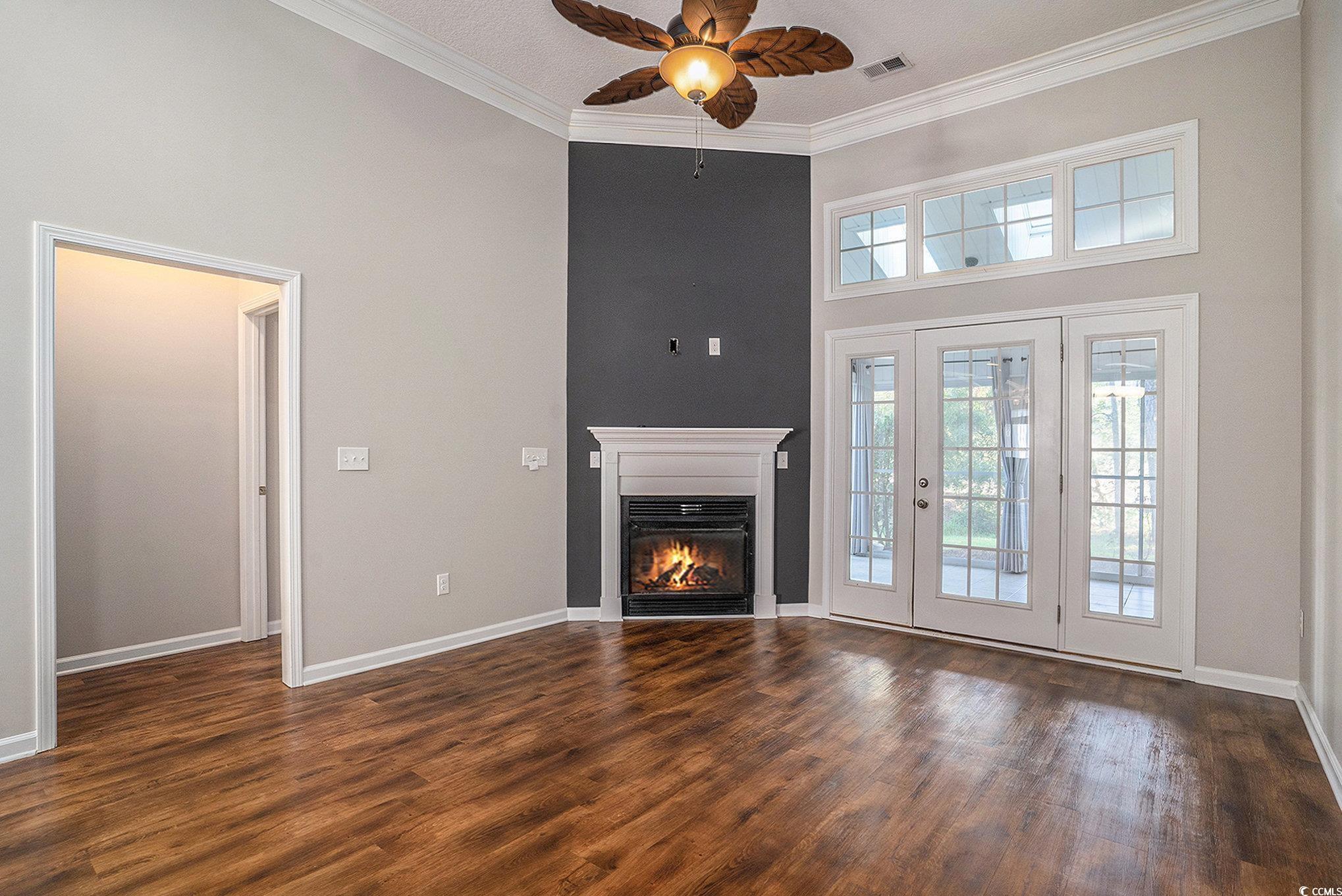 1018 Red Sky Lane, Unit 101 Murrells Inlet, SC 29576 - Photo 18 of 35 Unfurnished living room featuring a towering ceiling, ornamental molding, a glass covered fireplace, ceiling fan, and dark wood finished floors