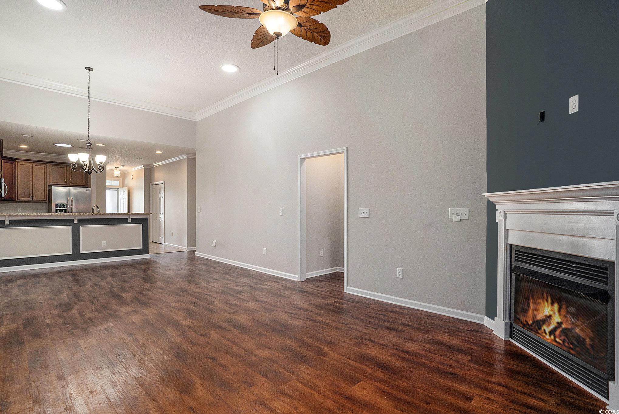 1018 Red Sky Lane, Unit 101 Murrells Inlet, SC 29576 - Photo 19 of 35 Unfurnished living room with ornamental molding, a glass covered fireplace, a chandelier, a ceiling fan, and dark wood-style floors