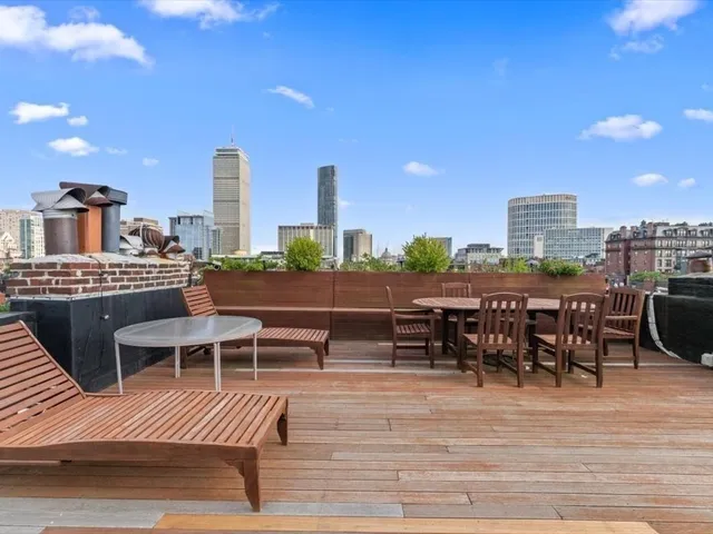 a view of a roof deck with table and chairs a barbeque with wooden floor and fence