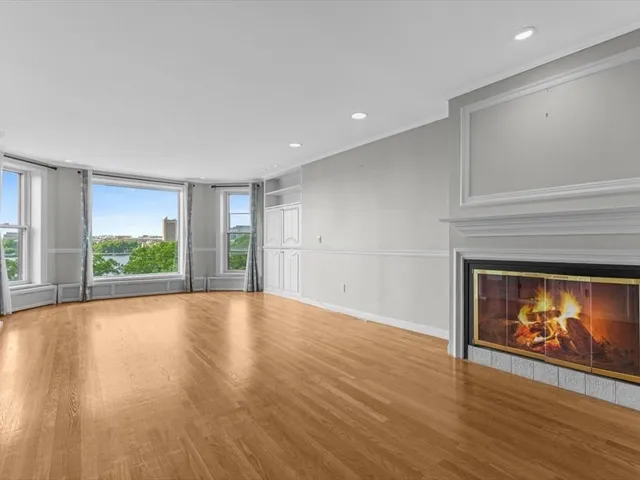 a view of an empty room with wooden floor fireplace and a window