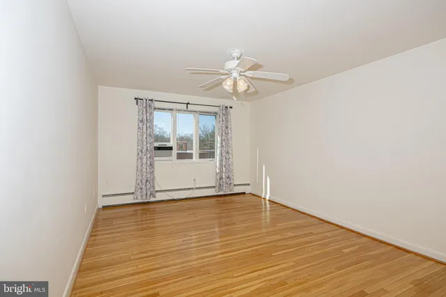 a view of an empty room with wooden floor and a ceiling fan