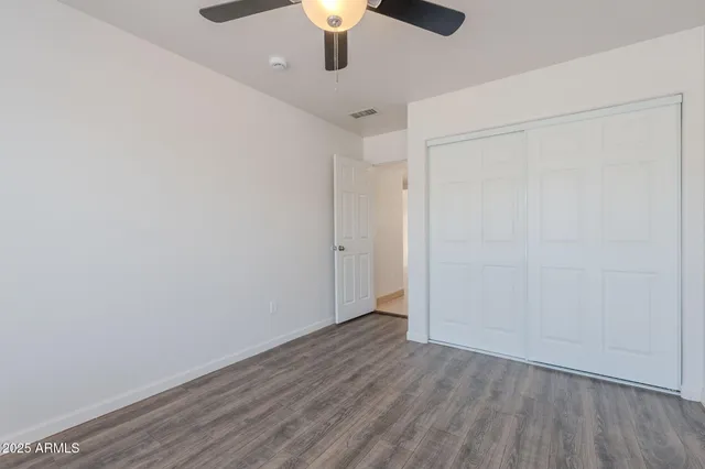 a view of an empty room with wooden floor and a ceiling fan