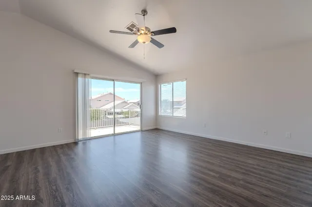 an empty room with wooden floor fan and windows