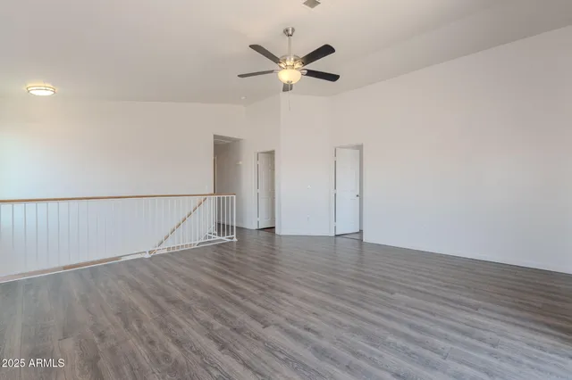 a view of an empty room with wooden floor and a ceiling fan