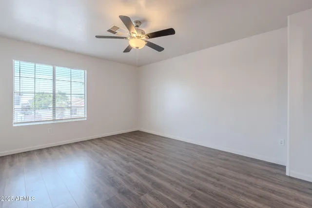 an empty room with wooden floor fan and windows