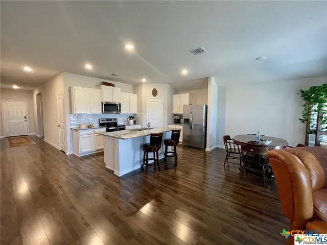 a kitchen with stainless steel appliances kitchen island granite countertop a stove a refrigerator a sink a dining table and chairs with wooden floor