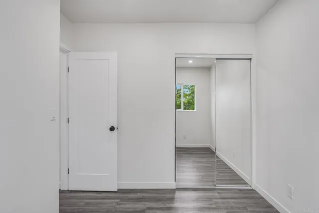 a view of an empty room with wooden floor and a mirror