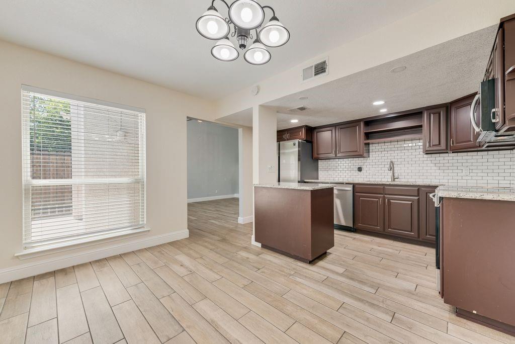 219 West Rochelle Road Irving, TX 75062 - Photo 8 of 29 Kitchen and dining area featuring wood-finish flooring, dark wood cabinetry, light granite-style countertops, white subway tile backsplash, and stainless steel appliances