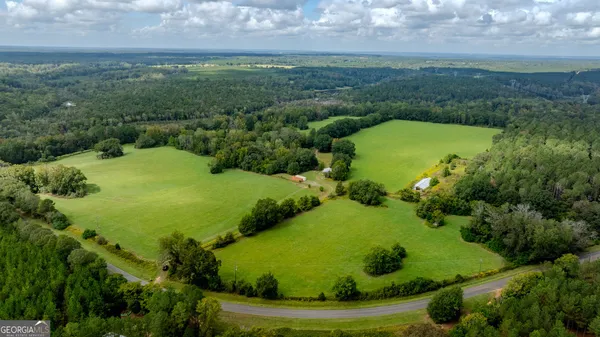 an aerial view of a residential houses with outdoor space and trees all around