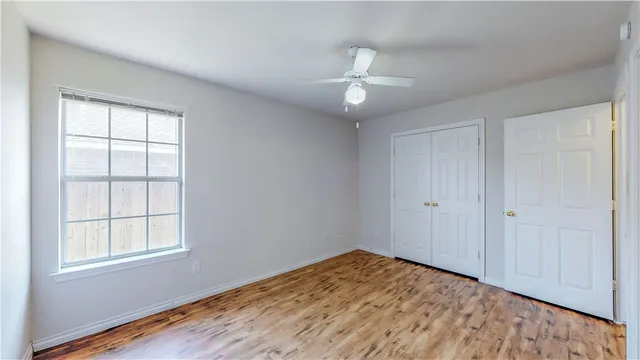 an empty room with wooden floor and way to kitchen